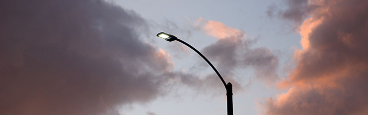 A streetlight illuminates against a backdrop of a cloudy sky at dusk.