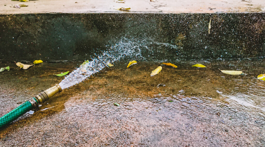 water hose turned on washing away leaves in the street