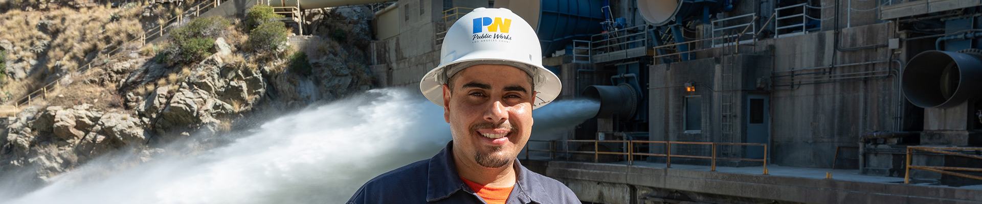 Employee wearing a hard hat standing in front of an open valve at a dam